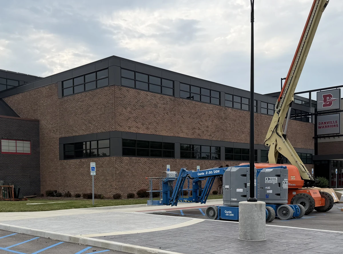 The corner of a two-story school after staining, the brick now a rich brown, two lifts still parked in the lot