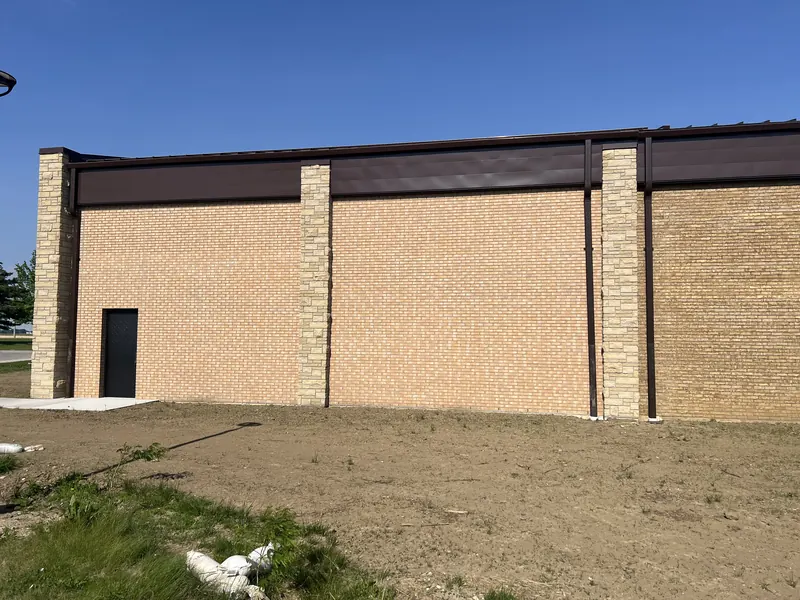 A commercial building where a new run of pink-toned brick meets the tan brick of the older wall at a stone pier