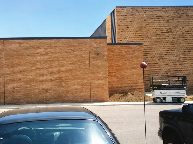 A low brick wall in one flat orange, beside a taller building whose brick runs a blended range of orange and dark units