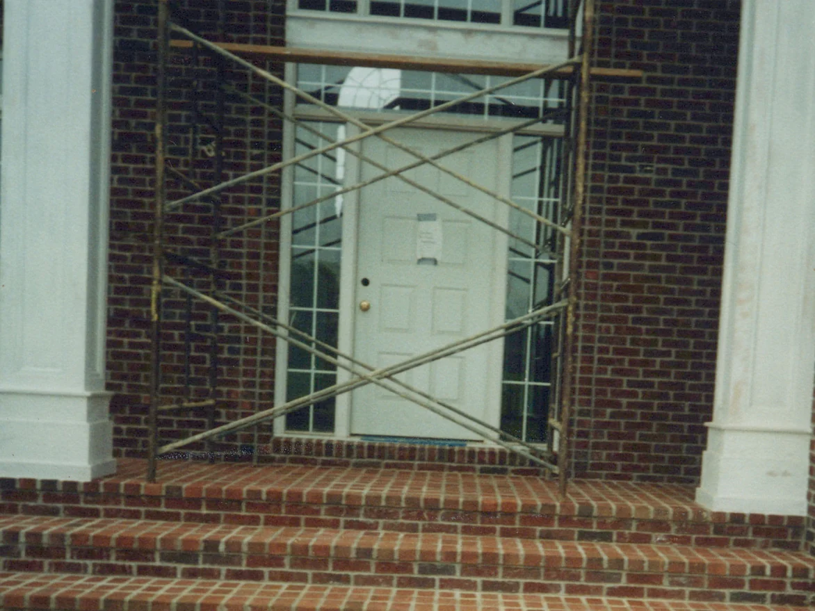 The whole entrance in 1998 after the pavers were darkened, three brick steps rising between two square white columns to a door with sidelights, a scaffold frame still standing in front of it