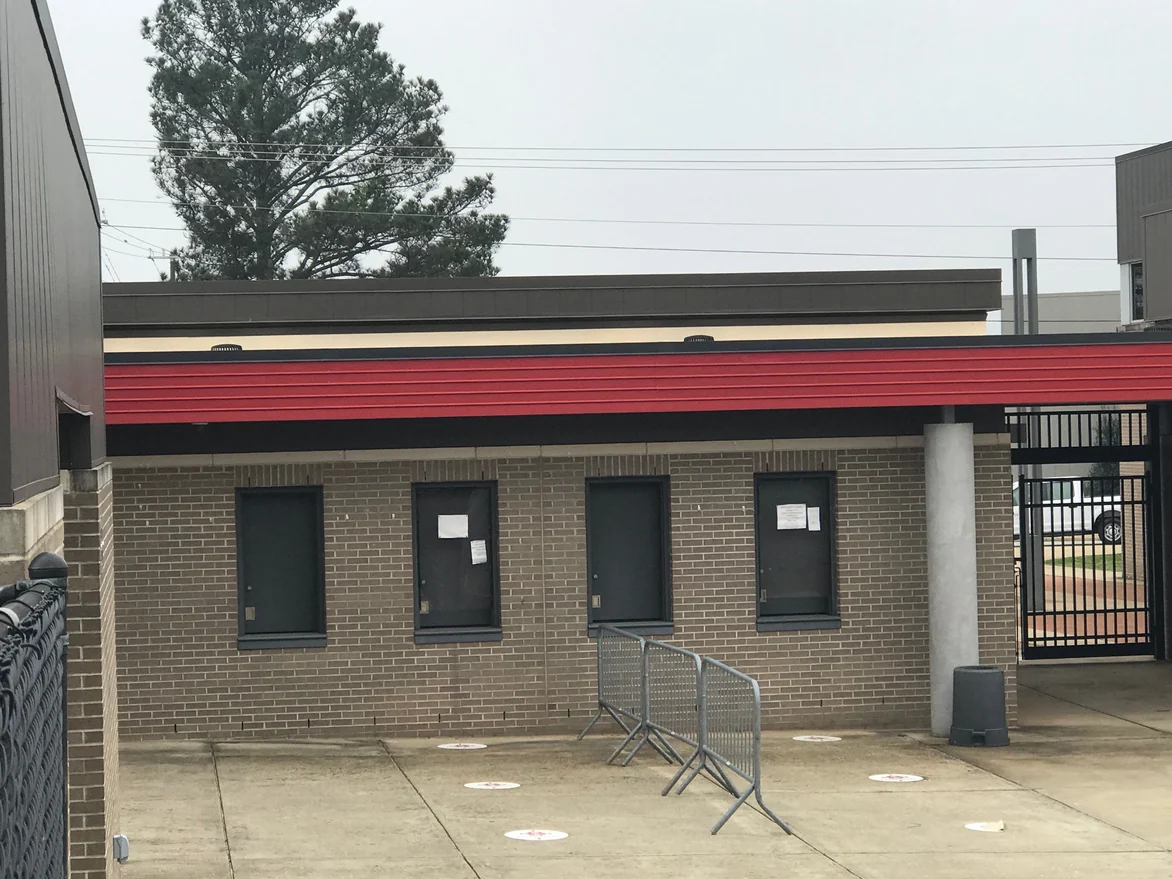 A low brick building on the stadium concourse in 2021, four shuttered service windows in tan brick with pale mortar joints under a red fascia