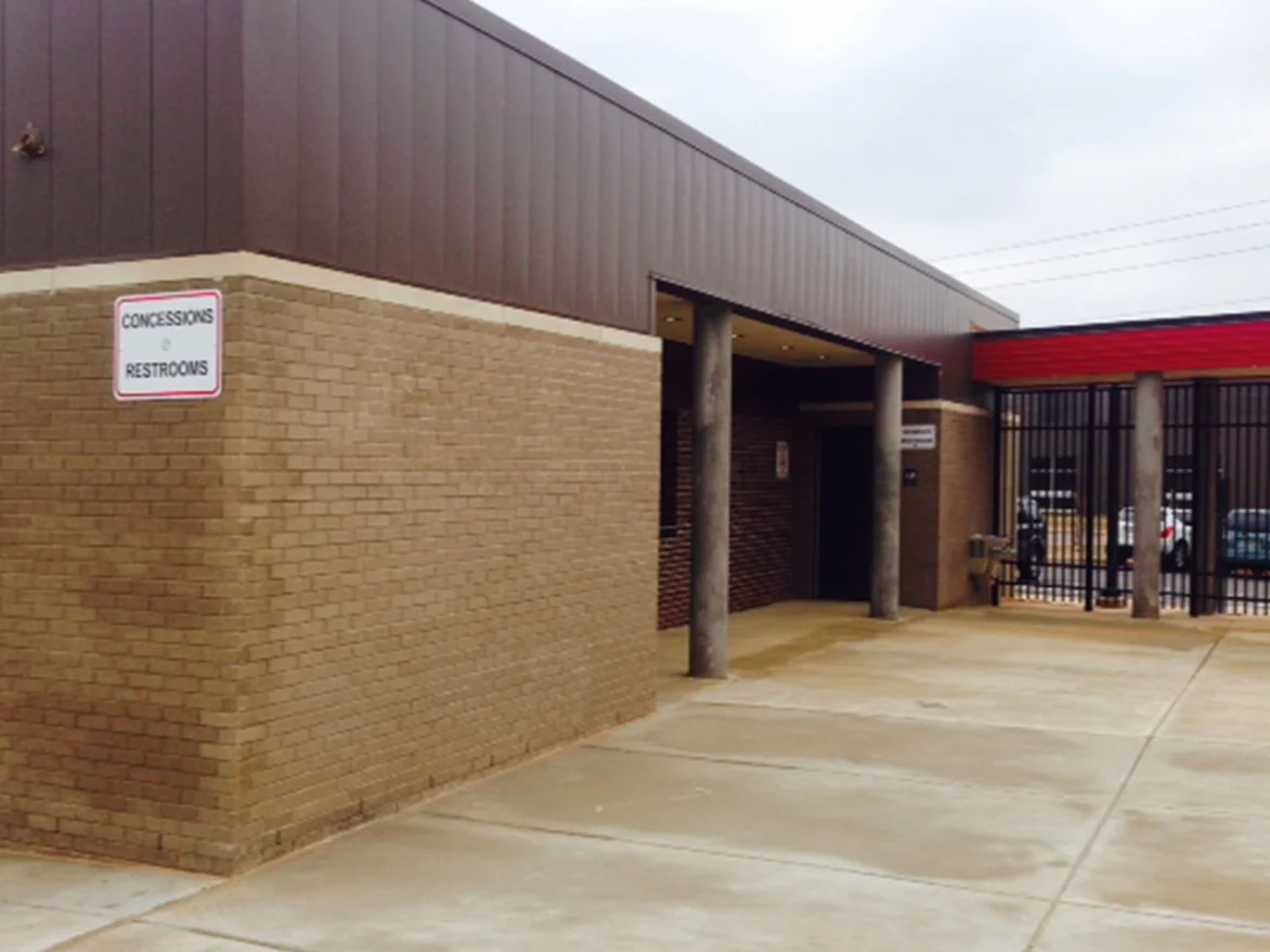 The concessions and restrooms building in 2014, tan brick under dark metal cladding with mortar joints running from grey to near black, a gated entrance beyond