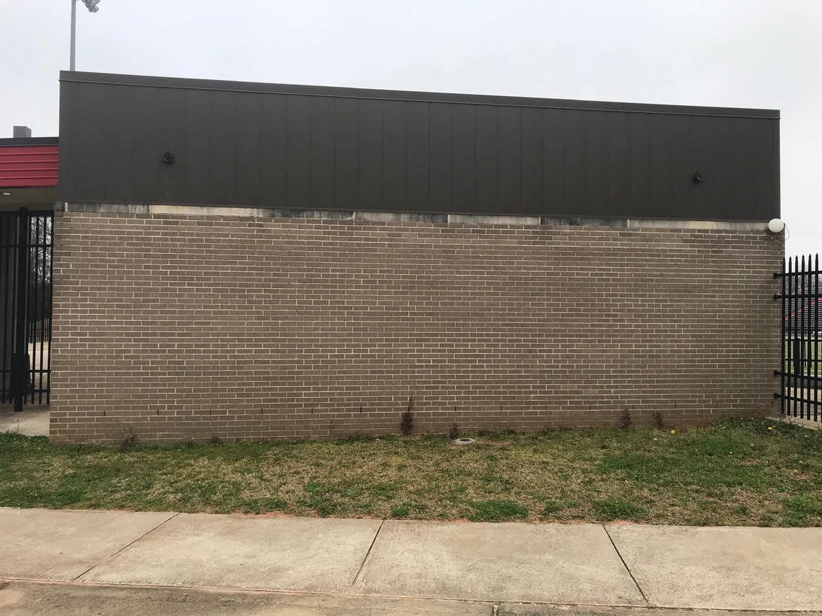 A brick wall between two steel gates at the stadium in 2021, tan brick with one pale mortar color from the stone cap down to the grass