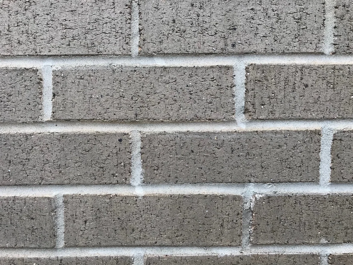 A close view of five courses of the brick in 2021, the mortar joints an even pale grey between textured grey-tan units