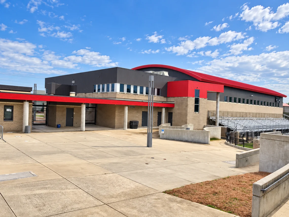 The stadium plaza in 2021, buff brick and stained mortar under the red fascia, the gates open along the concourse and the bleachers beyond