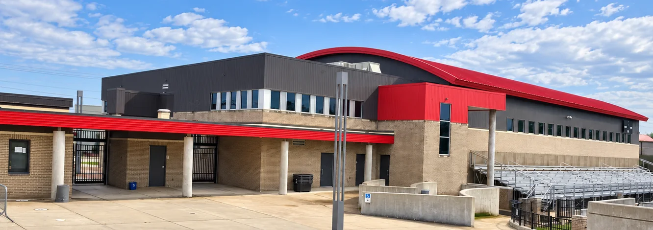 The stadium plaza at the Alabama high school in 2021, buff brick and stained mortar under the red fascia, with the bleachers beyond