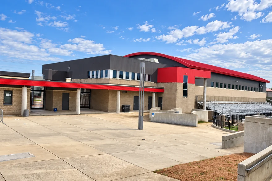 The stadium plaza at the Alabama high school in 2021, buff brick and stained mortar under the red fascia, with the bleachers beyond