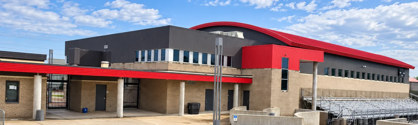 The stadium plaza at the Alabama high school in 2021, buff brick and stained mortar under the red fascia, with the bleachers beyond