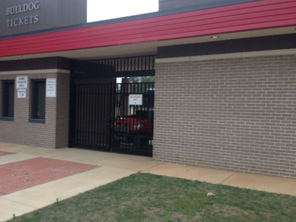 The home ticket booth and gate under a red fascia after staining, grey-tan brick with the mortar one pale color across the wall