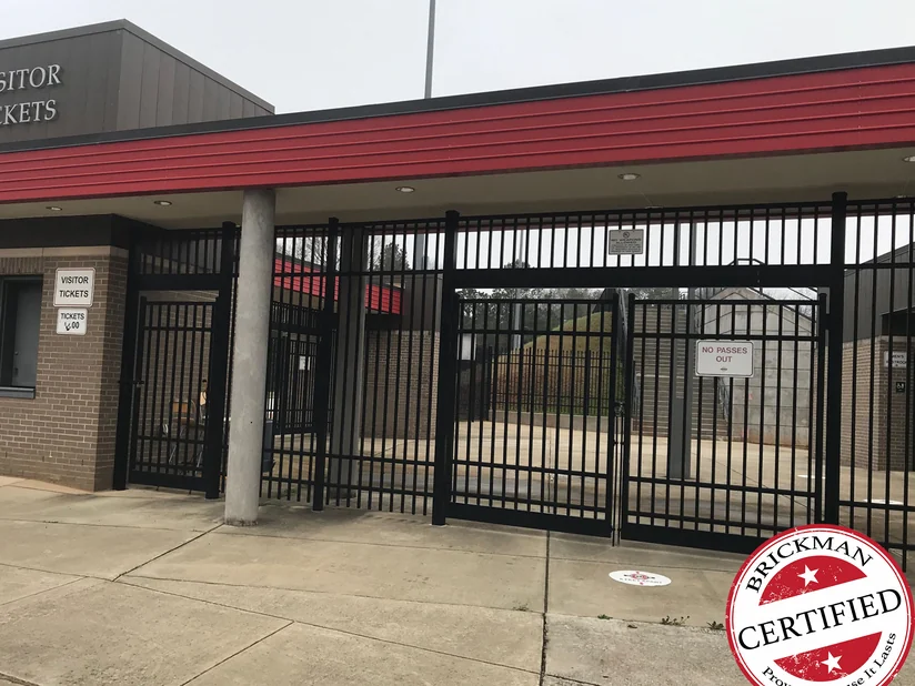 The visitor ticket gate in 2021, a brick booth with a ticket window beside steel picket gates under a red fascia, with the certification stamp in the corner.