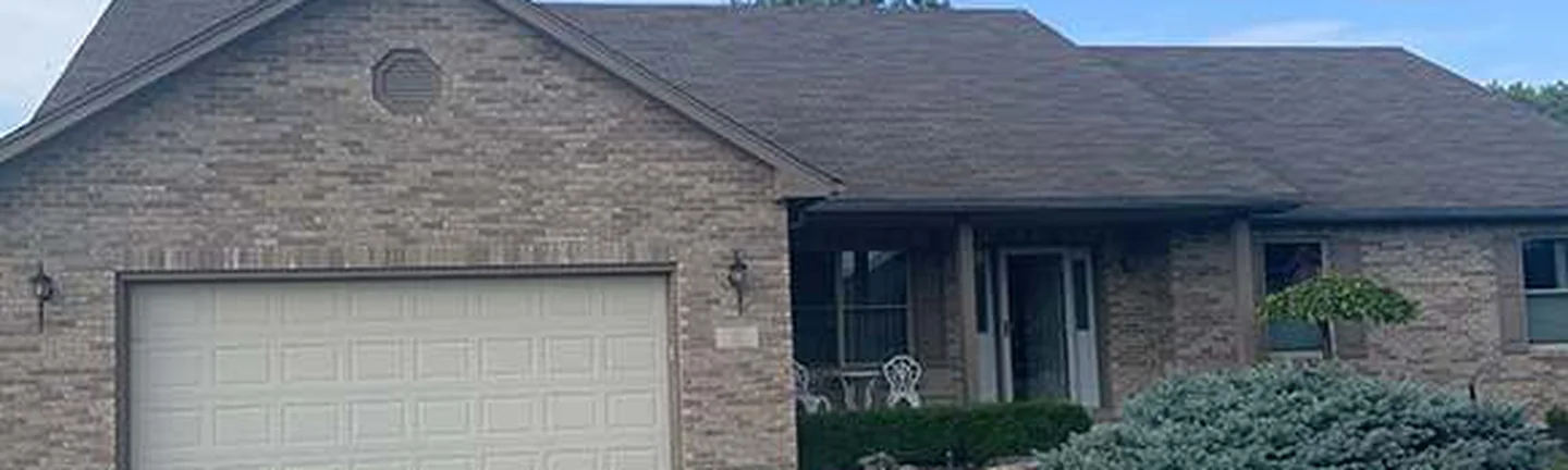 The front of the Arcanum house in 2019, buff brick running from the two-car garage past a covered porch