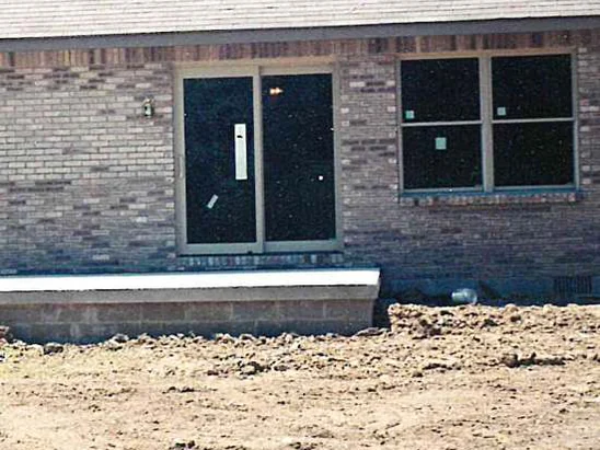 The patio door wall in 2000, the brick red brown around the door and lighter through the courses above it, with bare dirt up to the foundation