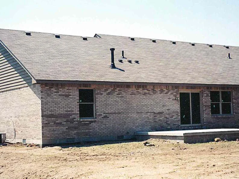 The back of the house in 2000, pale pink and cream brick blotched unevenly across the courses above bare graded dirt
