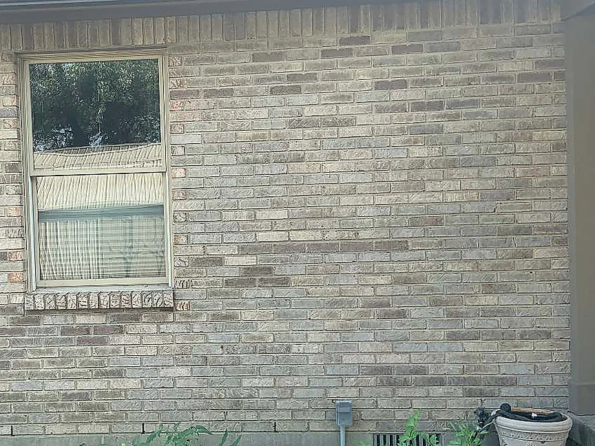 The same window in 2019, curtains behind the glass and a planter on the slab below, the brick holding a mixed range of tan, grey and mauve