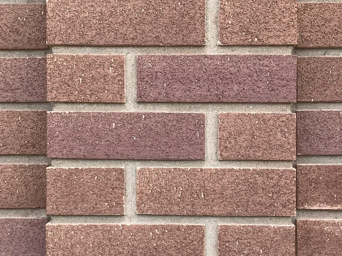 Close view of the brick at unit scale in 2019, rose, brown and mauve units in a running bond with a projecting course stepping out of the wall
