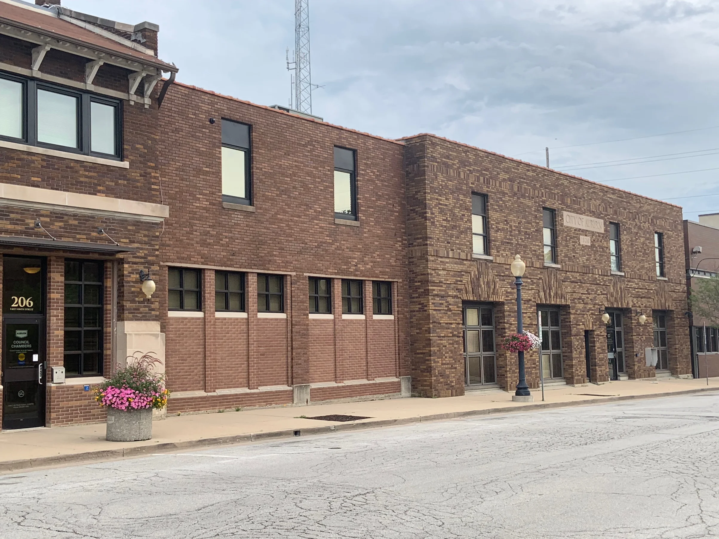 The city hall from across the street in 2019, a two story brick front running from the entrance canopy to a stone band lettered CITY OF AUBURN