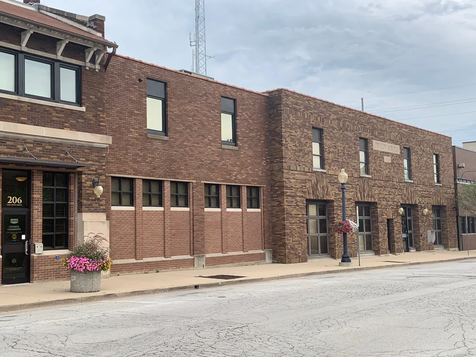 The city hall from across the street in 2019, a two story brick front running from the entrance canopy to a stone band lettered CITY OF AUBURN
