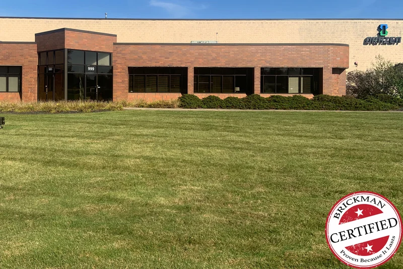 The front of the building in 2019 across a mown lawn, the entry and the run of window bays carrying one even darker red brick to the curved corner, with the certification stamp at the corner of the frame