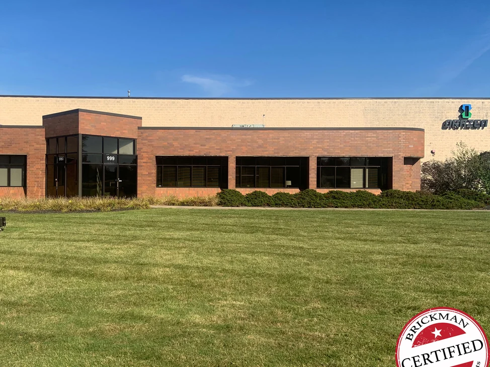 The front of the building in 2019 across a mown lawn, the entry and the run of window bays carrying one even darker red brick to the curved corner.