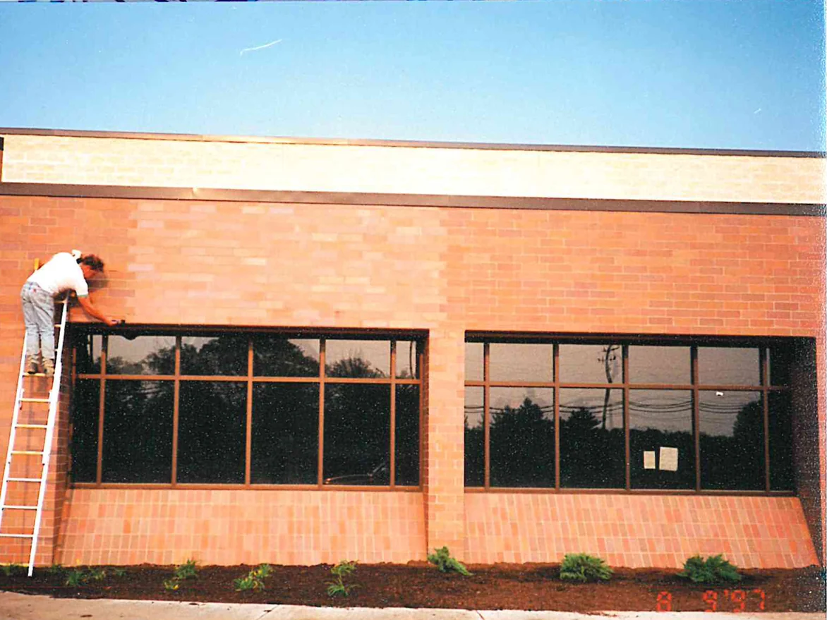 An applicator on a ladder working across the brick above a window bay in 1997, the wall a pale salmon orange with a band of cast stone above it