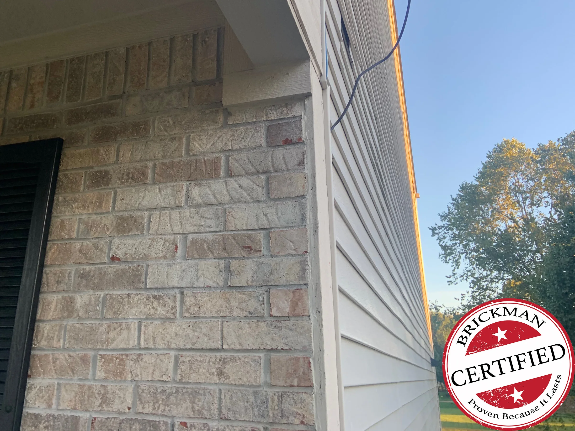 The same outside corner in 2019, the brick reading as one buff and tan range where it meets white lap siding, with the certification stamp at the lower right