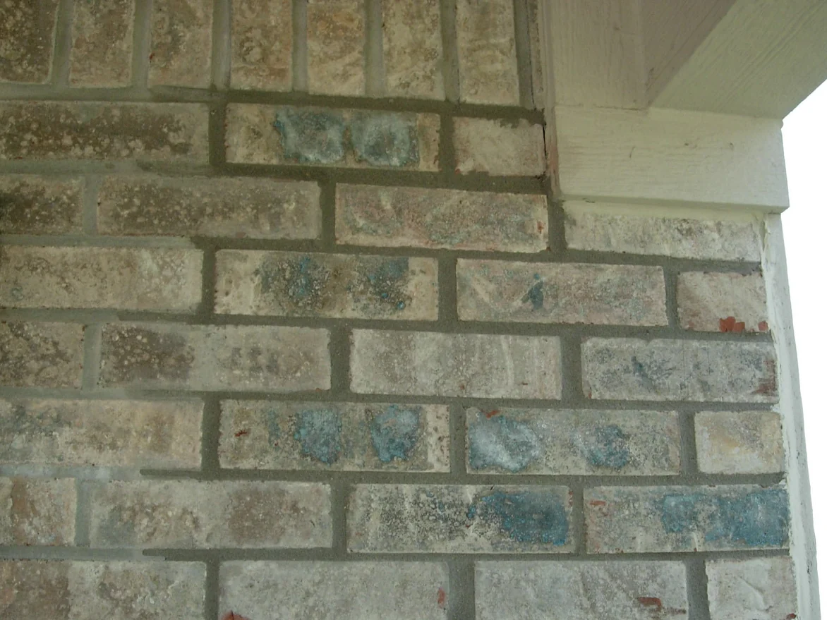 An outside brick corner beside a shuttered window in 2007, several units across the wall carrying a blue-grey mottle that stands out from the buff and tan around them