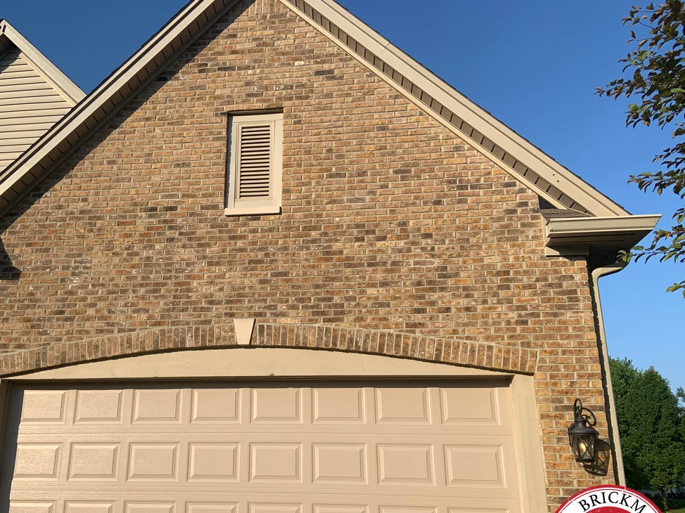 The gable end of an Avon, Indiana home in 2019, the brick an even tan and brown range from the peak down to the arch over the garage door, the Brickman certified stamp entering the bottom corner of the frame.