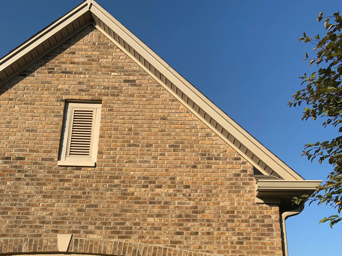 The gable seen from below in 2019, the raking eaves and the attic vent above a soldier course arch, the brick one consistent range