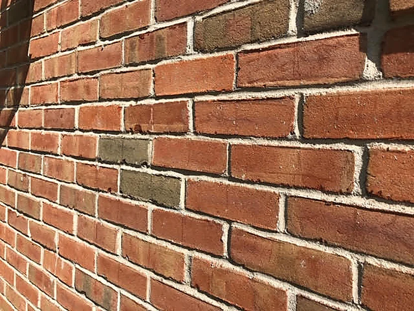 The wall at unit scale in 2019, seen along the brick at a raking angle, reds, tans and olive browns with pale mortar joints