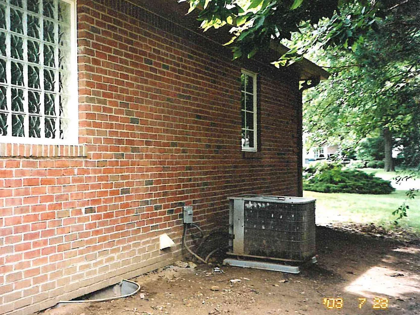A side wall of the same house in 2003, red and brown brick running back from a glass block window to an air conditioning unit at the far corner