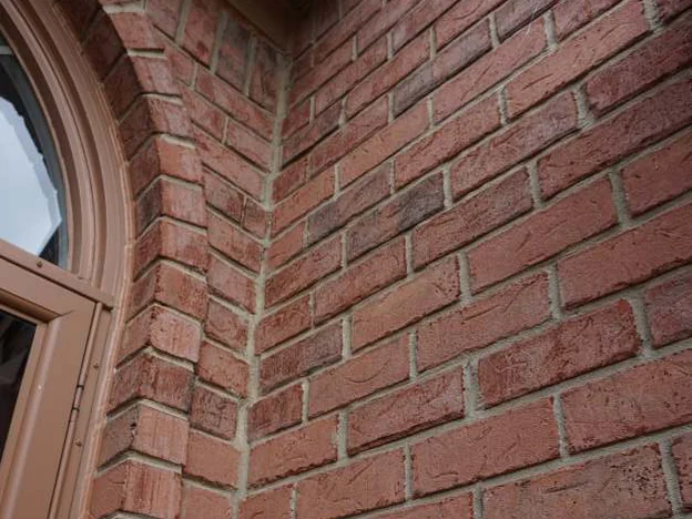 The brick beside the arch of the front door in 2019 at close range, courses of orange-red units meeting at the corner under tan trim