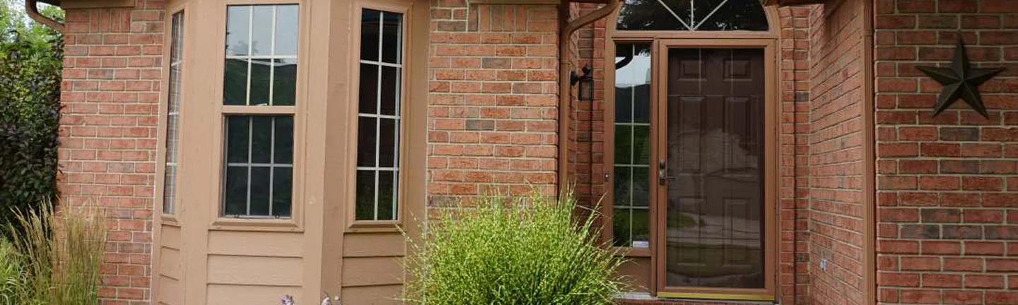 A wide band across the front of the house in 2019, orange-red brick around a bay window and an arched front door under tan trim