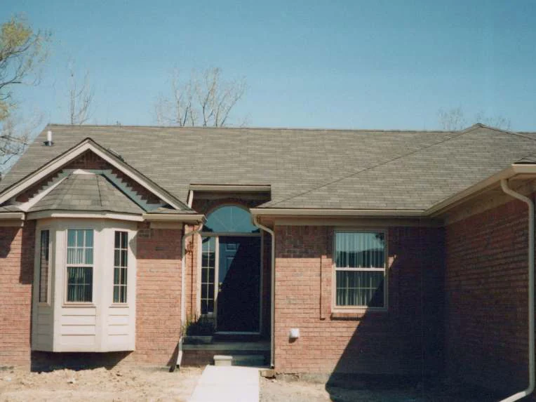 The front of the house later in 1998, the bay window and arched entry under the same roof, the brick reading darker and more even across the elevation, the ground still bare