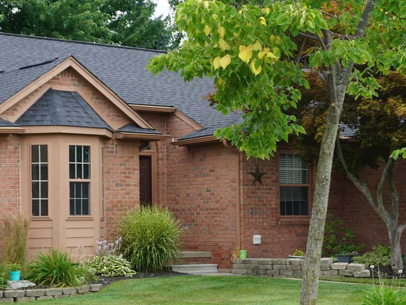 The front of the house in 2019 from the lawn, the bay window and entry under mature trees, the brick one even range across the elevation