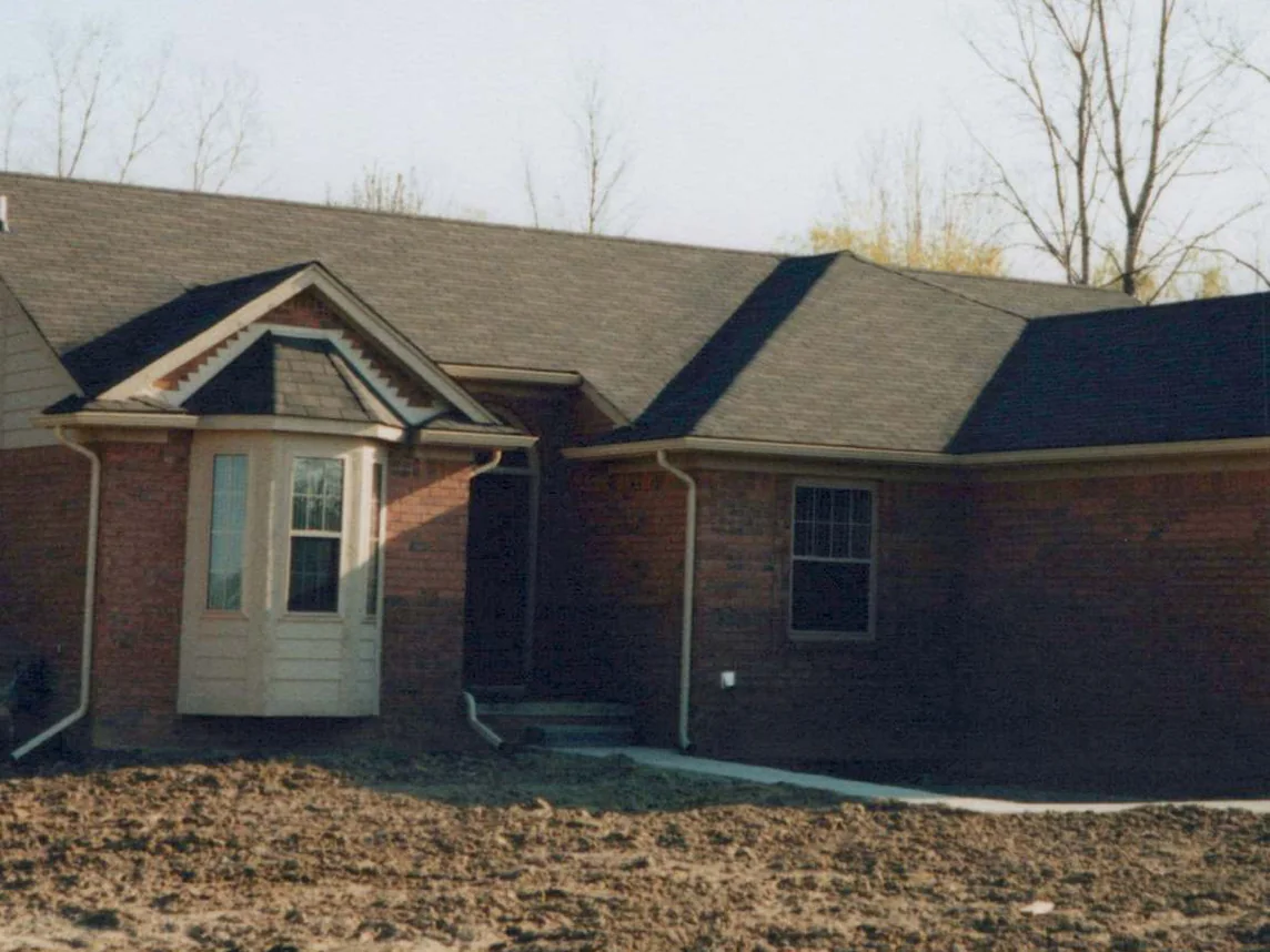 The front of the house in 1998 with the brick newly laid, cream trim on the bay window, bare trees behind the roof and raw graded earth where the lawn will be