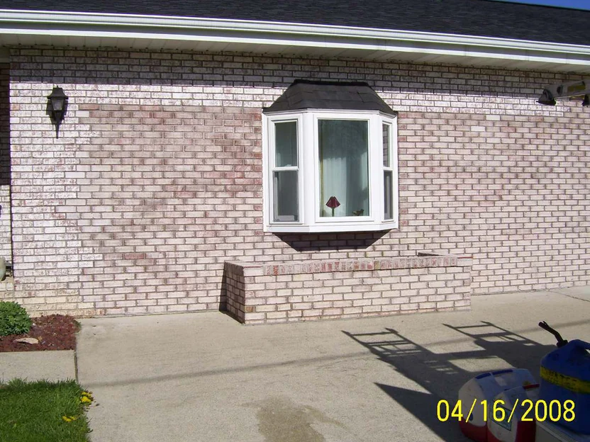 The front wall beside the bay window in 2008, white coated brick broken up by red and purple units, photographed with a burned-in date of 04 16 2008