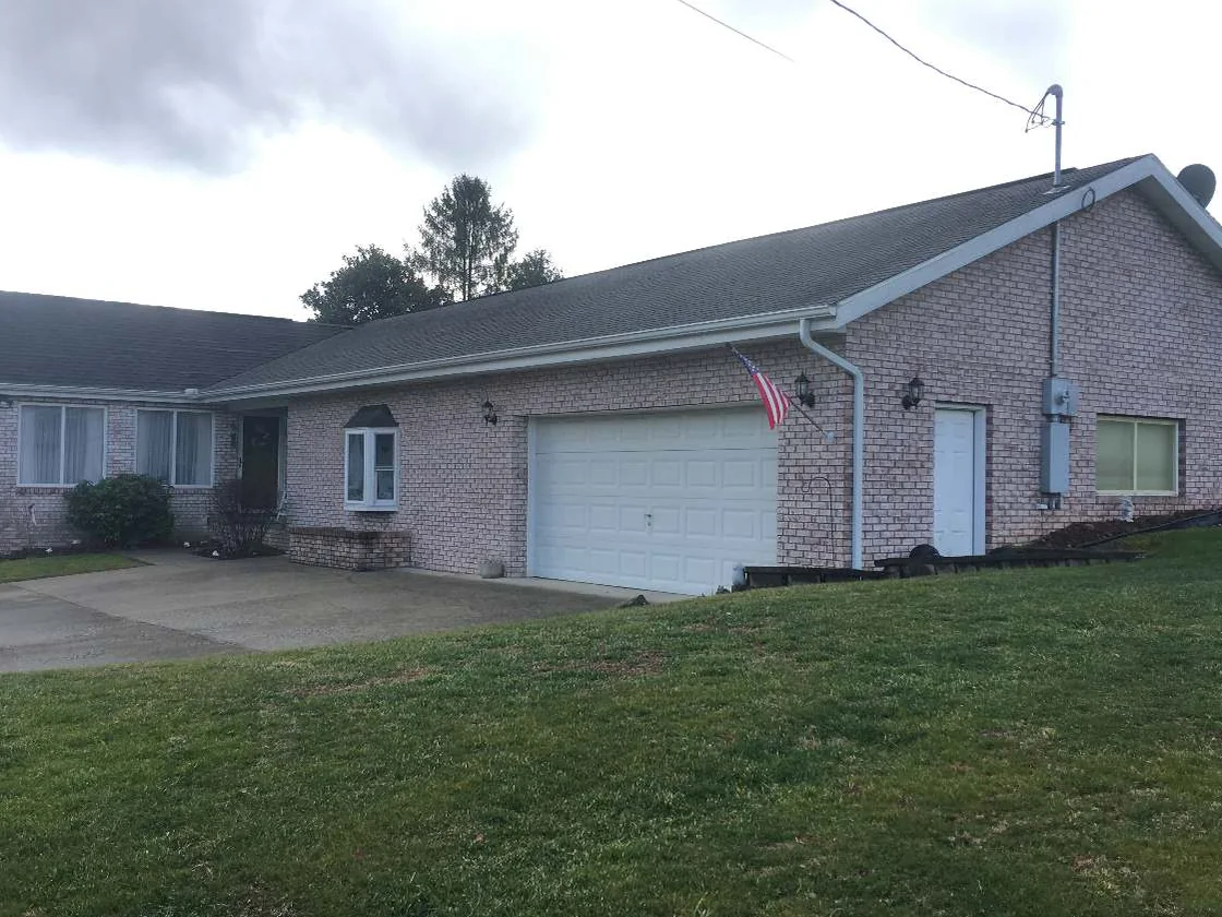 The whole front of the house in 2020, pale pink brick running from the bay window past the entry to a white garage door, lawn mown to the drive
