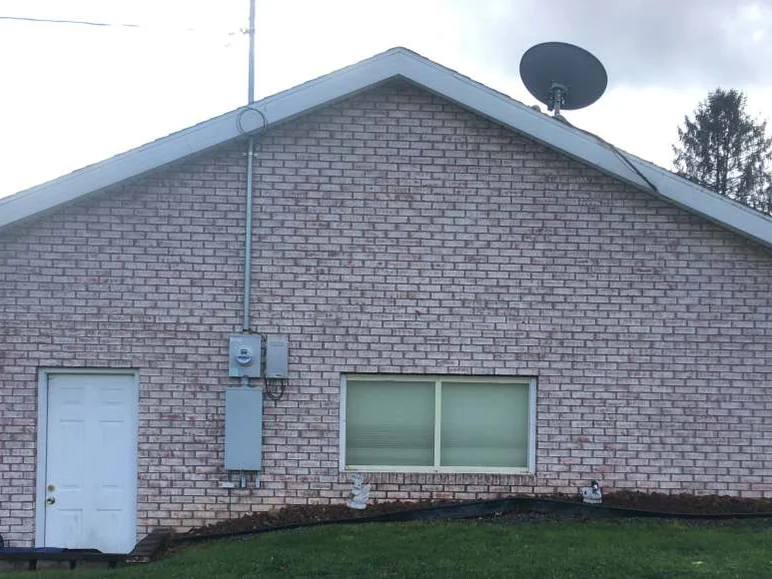 The gable end in 2020, the same pale range across the wall, with a meter box added and landscape timbers and turf where the bare dirt had been