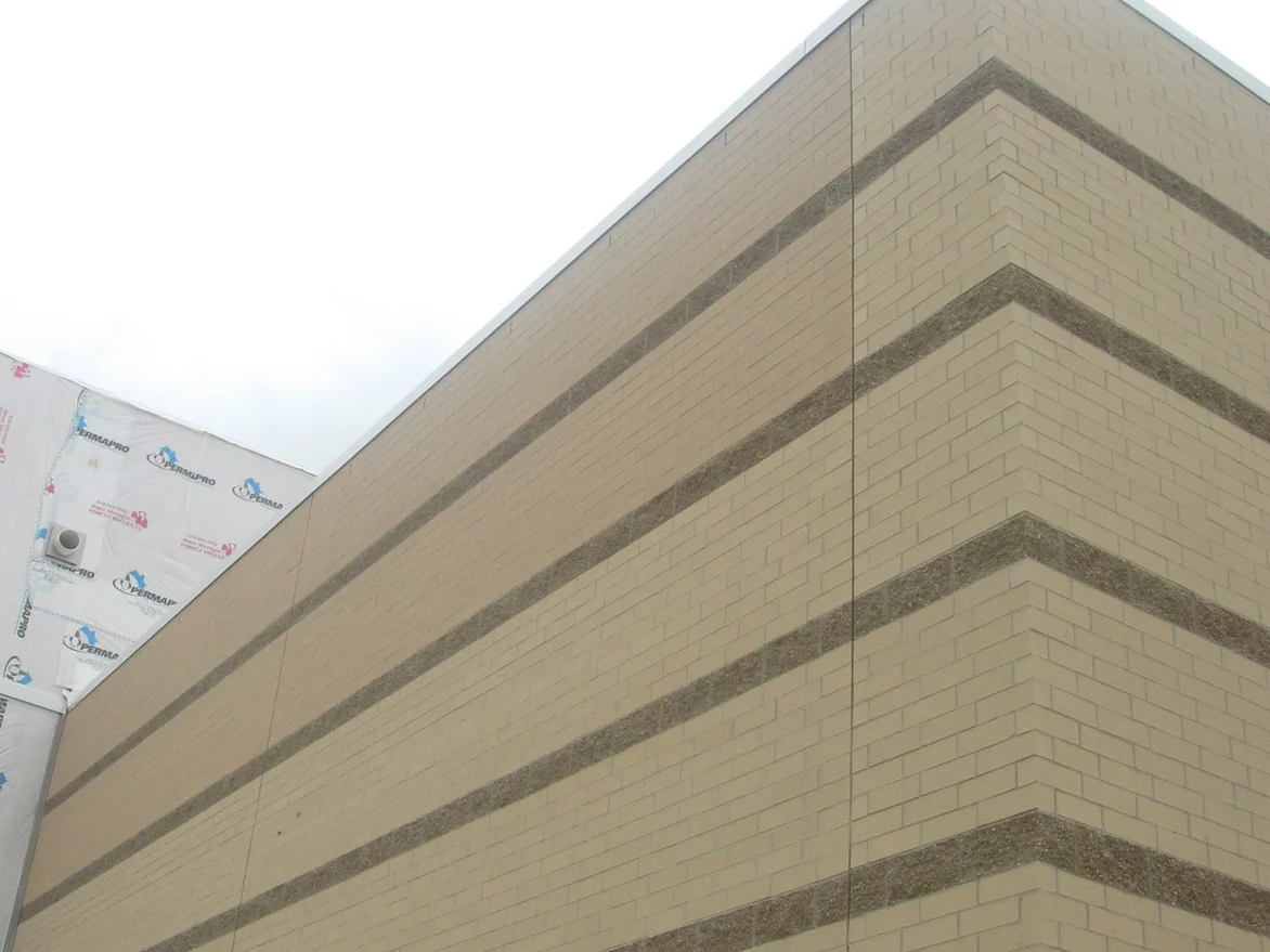 An outside corner of the buff brick wall before staining, the two accent bands nearest the parapet a distinctly darker brown than the bands running below them