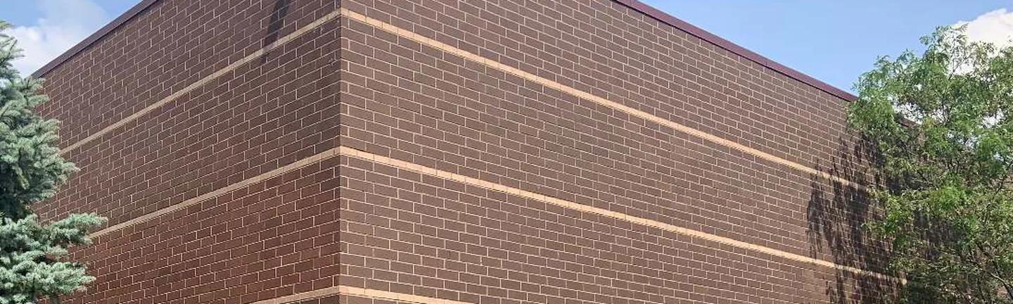 The outside corner of the store in 2019, dark red brown brick running past four cream accent courses to a metal parapet