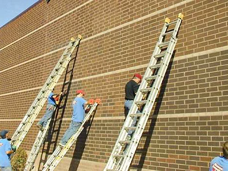 Five applicators working the end wall in 2002 from three extension ladders, the brick to the left of them already lighter than the brick to the right