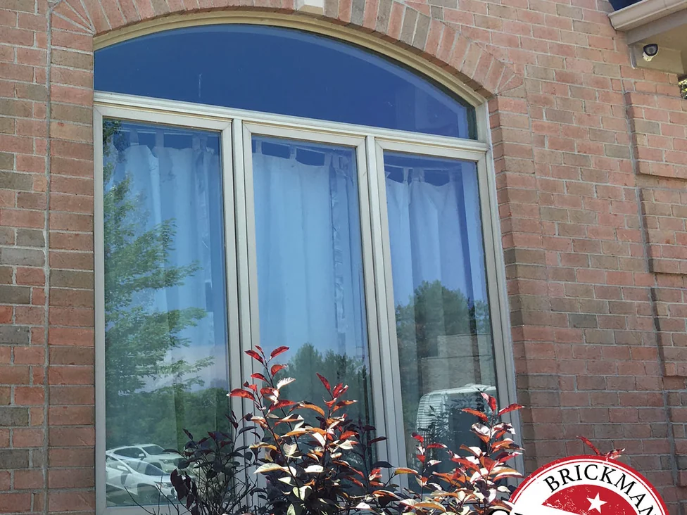The same arched front window in 2019, the brick of the arch and the wall around it holding one even range of red, tan and grey