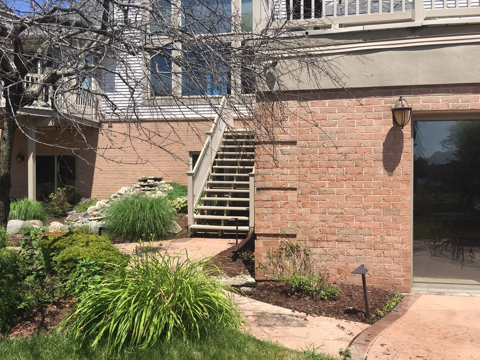 An outside corner of the walkout level in 2019, the brick turning the return in one range from the path to the underside of the deck