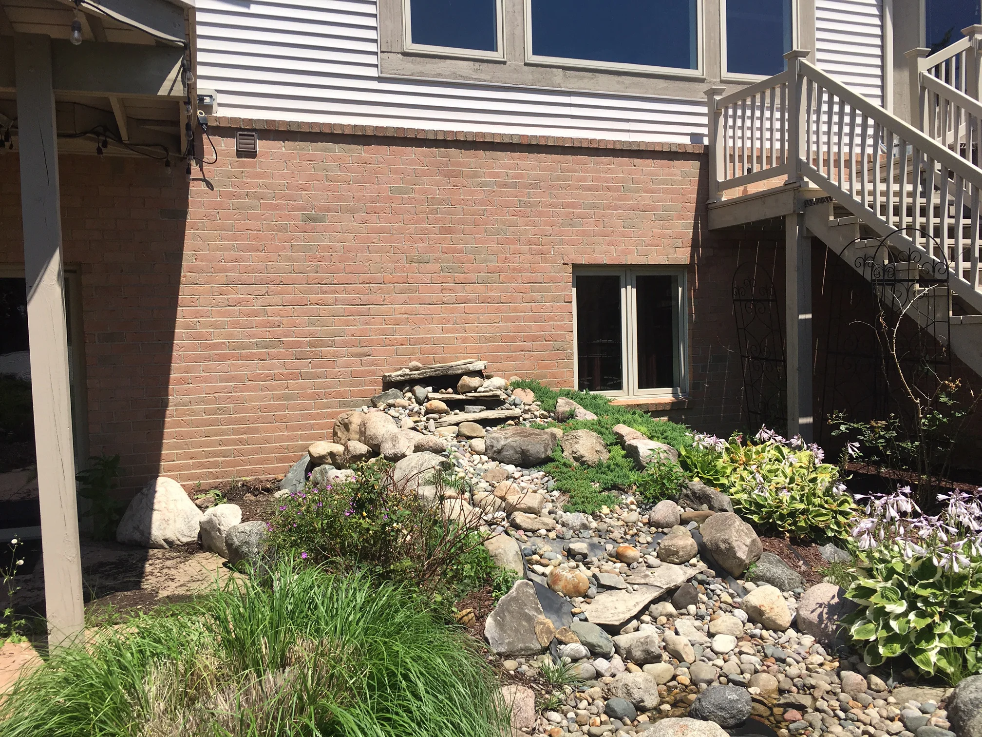 The walkout wall in 2019 seen across a rock garden, one range of red and tan brick running its full length below the sided upper story