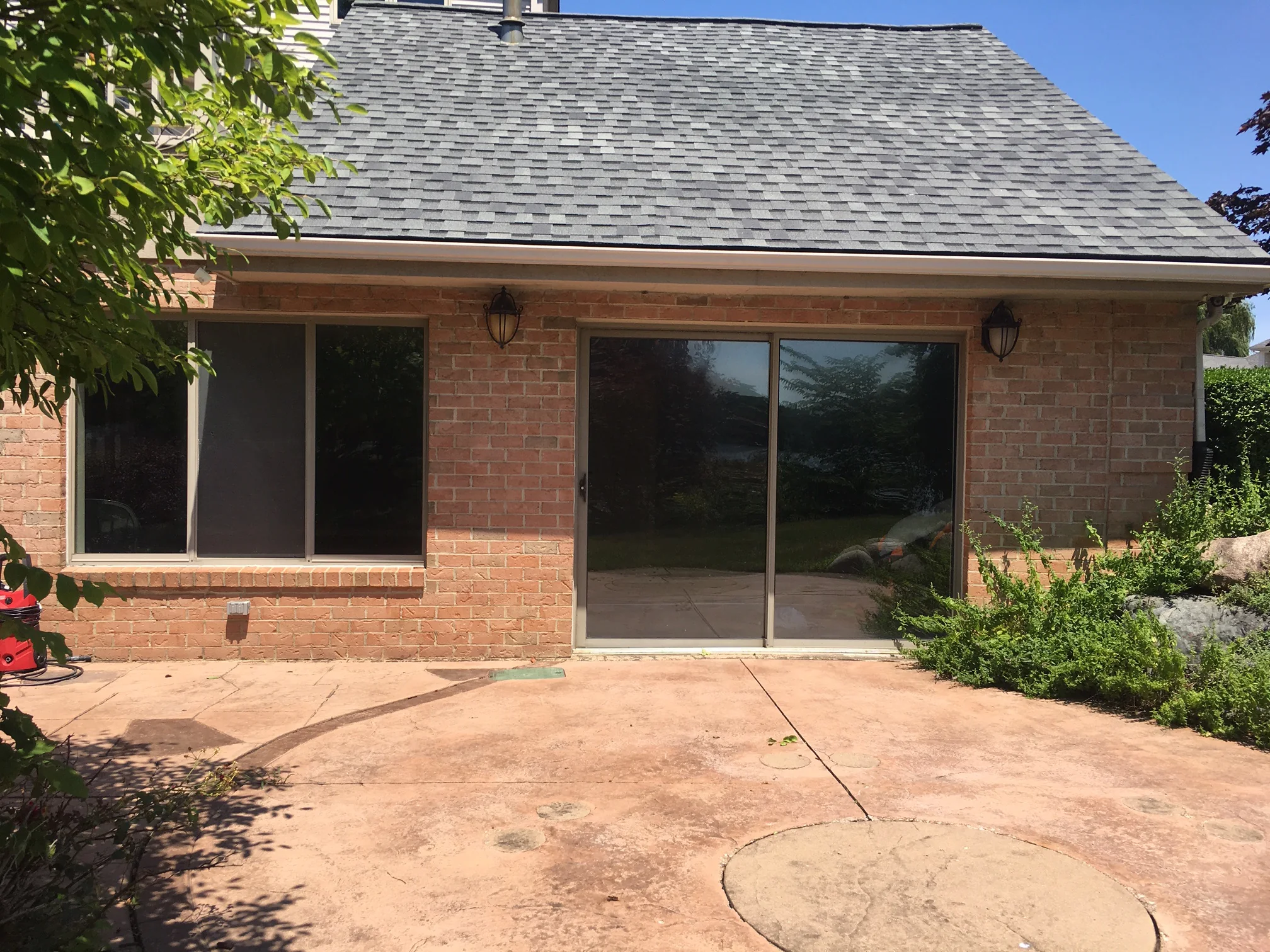 The rear wing of the house in 2019 from the patio, its brick one even range of red and tan under a shingled gable, with a sliding door between two lanterns