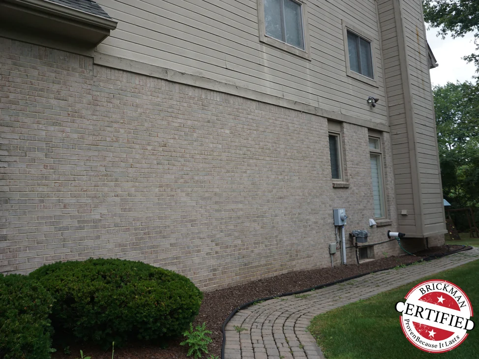 The long side of the house in 2019, its brick one even light buff range, with clipped shrubs and a paver path running along the wall