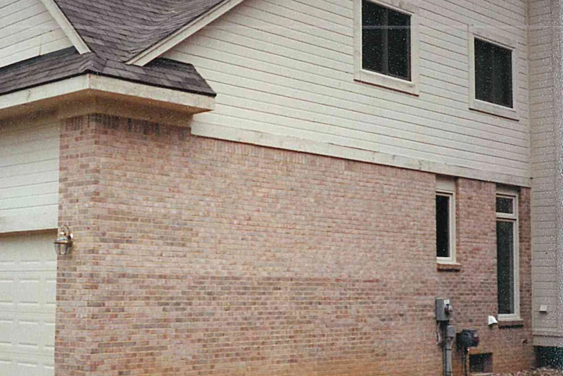 The long side of the house in 1997, its pinkish tan brick carrying darker blotches and bands through the courses, the ground around it still bare from construction