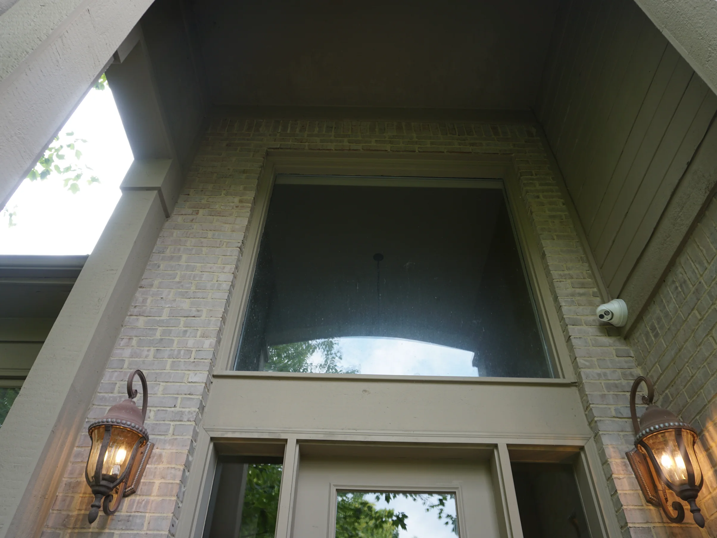 Looking up into the two-story entry, the brick jambs and the header course around the tall window in one even buff range, a lantern on each side