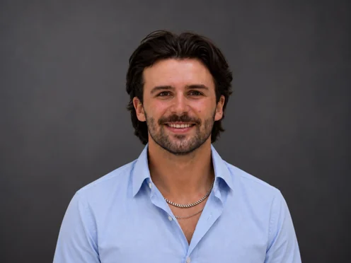 Harrison McCoy in a light blue shirt against a dark grey studio backdrop