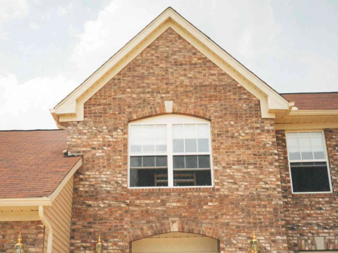 The front gable of the house in 1997 before the correction, blended tan and orange brick around an arched window, with patches of paler brick standing out near the peak of the gable and beside the entry arch